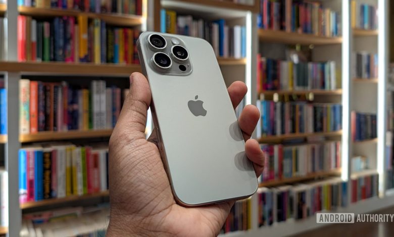 Apple iPhone 16 Pro in Natural Titanium color held out in hand, against the backdrop of books