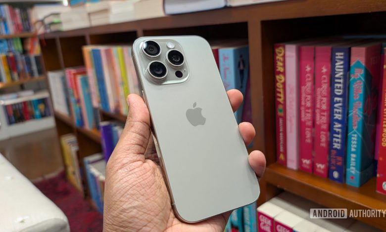 Apple iPhone 16 Pro in Natural Titanium color held out in hand, against the backdrop of books