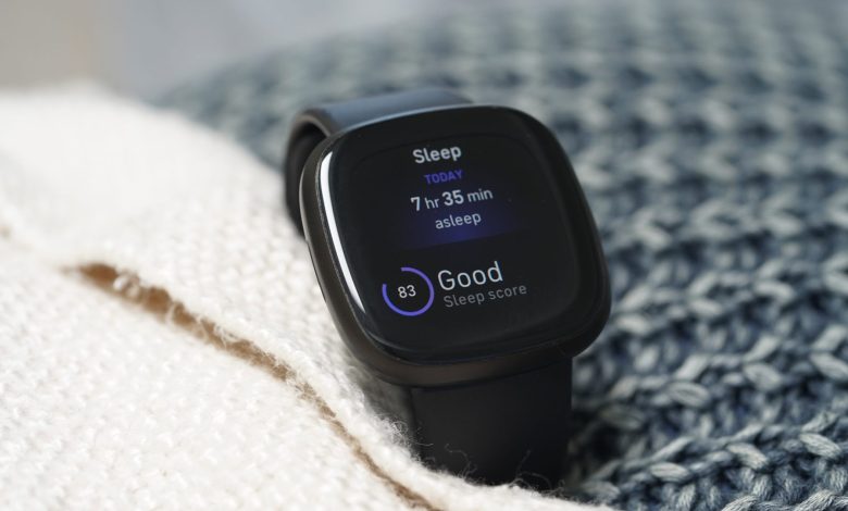 A Fitbit Versa 3 rests in a pile of bedding, displaying a user's sleep data.