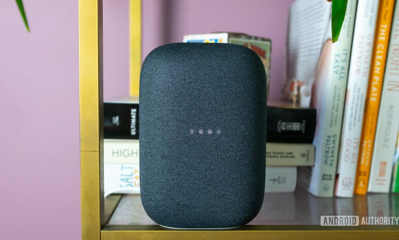 Pictured is the gray Google Nest Audio on a bookshelf with the lights blinking.