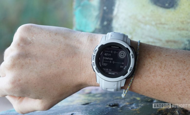 A Garmin Instinct 2S on a user's wrist displays the device's built-in compass.