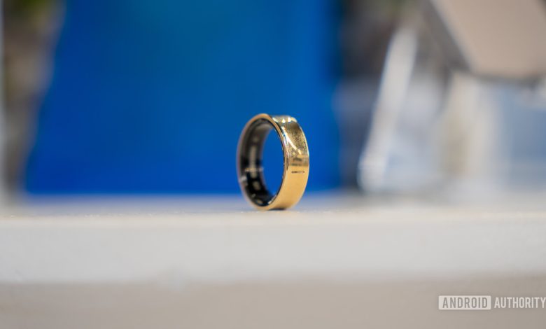 A Gold Titanium Samsung Galaxy Ring rests on a white surface.